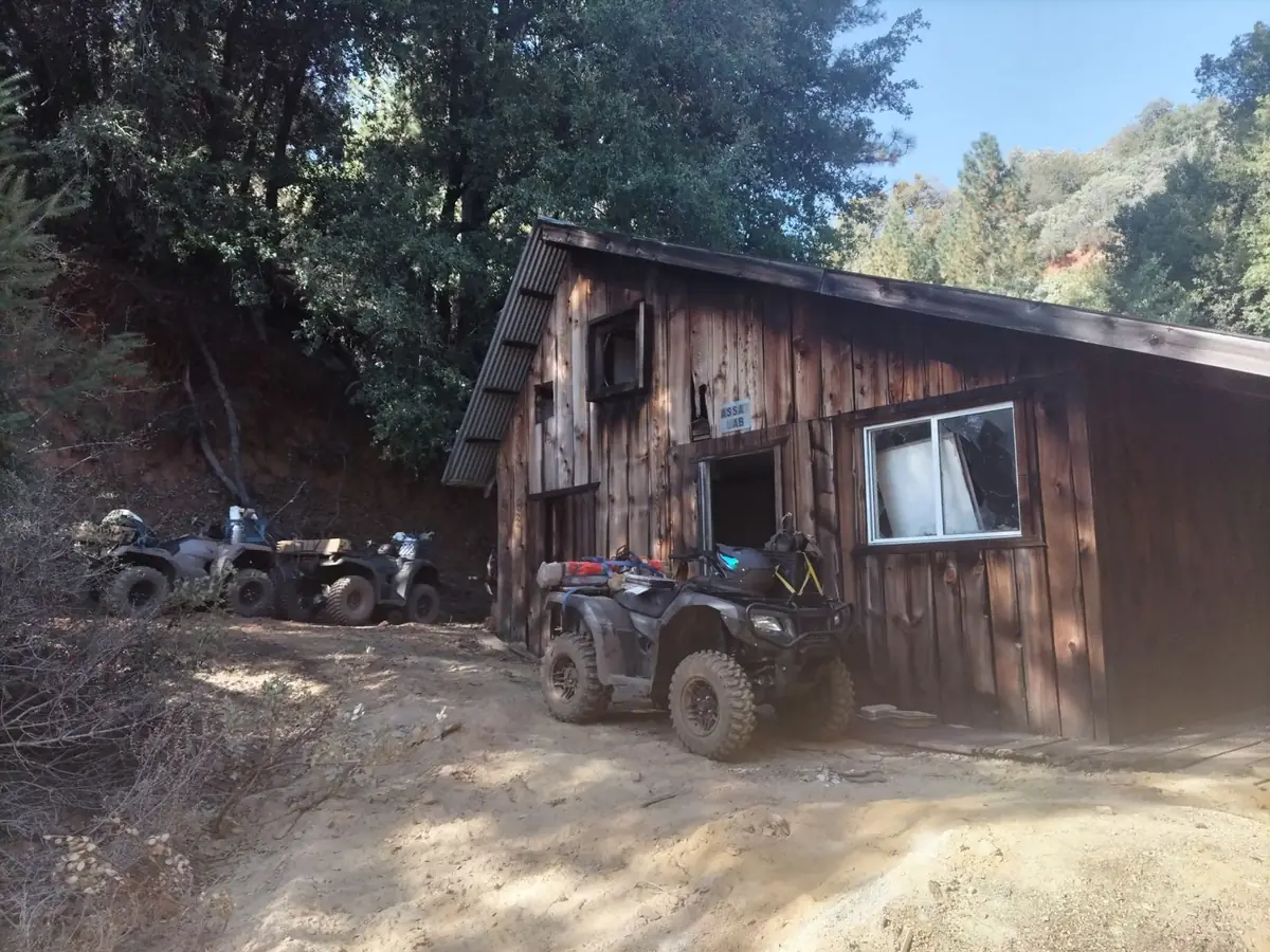 Field crew all-terrain vehicles parked beside a weathered wooden building marked Assay Lab, in steep, wooded terrain on the Buckingham claims in Mariposa County, California